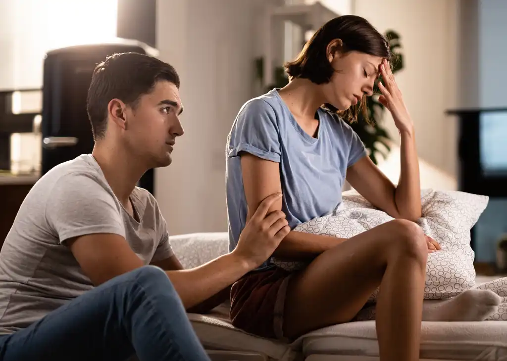 A couple sitting far apart on a couch, representing the relationship intimacy problems and anxiety that can be linked to Erectile Dysfunction (ED).